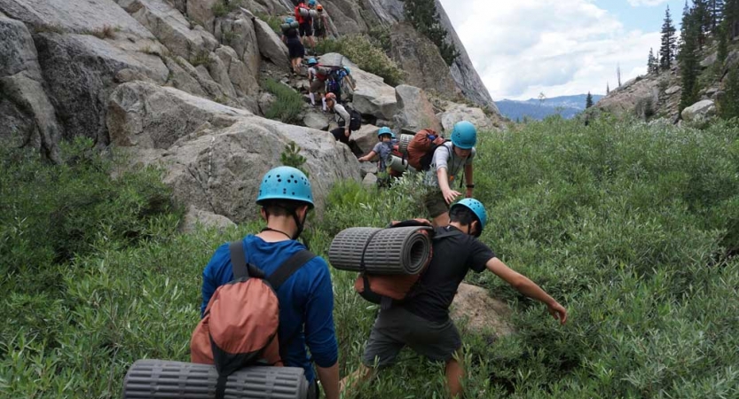 A group of people wearing helmets traverse over a rock formation 